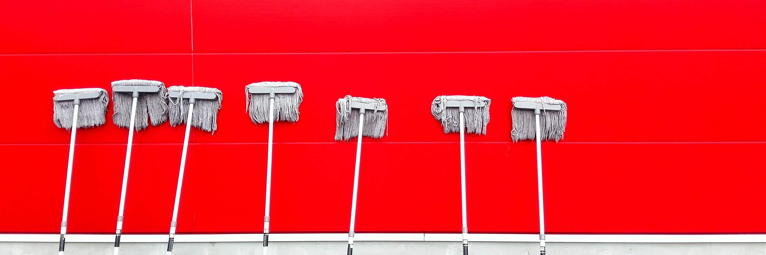 7 Wischmopps aufgereiht an einer roten Hauswand